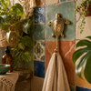 Brass sea turtle wall hook displayed on a Mediterranean tiled wall with plants and a towel, coastal ocean animal decor.