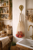 Handmade brass sunflower wall hook holding a mesh produce bag in a cozy cottagecore kitchen with farmhouse sink and natural wood accents.