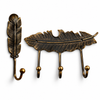 Antique brass feather wall hook set of 2 on a white background: one single feather hook with a ball-tipped hook and one 3-hook feather coat rack, both in a darkened aged brass finish. Handmade cast brass entryway, coat and towel hooks, hand-cast and finished by artisans in Ubud, Bali.