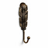 Single antique brass feather wall hook on a white background, in a darkened aged finish that brings out the carved feather texture, with a ball-tipped curved hook. Handmade cast brass coat and towel hook from Ubud, Bali, part of the antique brass feather wall hook set of 2.
