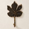 Brass maple leaf hook in a dark antique finish on a cream background
