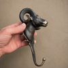 Full length view of antique brass ram wall hook held in hand showing complete sculptural profile from horns to hook — decorative gothic wall hook handmade in Ubud Bali