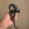 Three-quarter view of antique brass ram wall hook held in hand showing full sculptural form including horns face and hook — gothic wall hook handmade in Ubud Bali