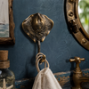 Antique brass stingray wall hook mounted on a blue bathroom wall holding a towel, vintage nautical hook from the coastal hook set.