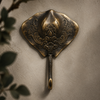 Antique finish brass stingray wall hook mounted on a textured wall with greenery, showing the vintage patina from the hook set.