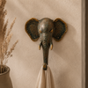 Close-up of patina brass elephant wall hook styled beside dried pampas grass on warm neutral boho wall showing verdigris patina finish and golden tusk detail in wabi sabi interior setting. Handcrafted decorative coat hook and towel hook from set of 4 for boho home decor, wabi sabi decor, yoga room decor and meditation space decor. Unique boho housewarming gift and eclectic gallery wall hook