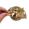 Gold brass bat door knocker held by a hand on a white background