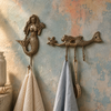 Brass 3-hook mermaid wall hook mounted on a textured wall holding a towel, coastal nautical towel hook.