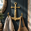 Brass anchor wall hook mounted on a dark blue wall near a round porthole mirror, holding a striped towel and woven bag, vintage maritime wall decor