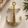 Brass anchor wall hook mounted on a cream wall near a plant, boho coastal maritime wall decor