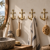 Brass anchor wall hook set mounted in a row in a boho bathroom, holding striped towels and a bath brush, coastal nautical bathroom decor