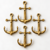 Set of brass anchor wall hooks arranged in a cluster on a cream surface, nautical coat hook set for maritime coastal decor