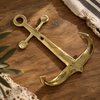 Brass anchor wall hook laid on a wood surface with striped linen fabric nearby, nautical brass hardware coastal decor