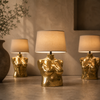 
Two small brass female torso sculptures used as matching lamp bases in a warm interior — gold body art lamp base decor for after dark decor and maximalist eclectic home decor