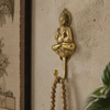 Gold brass sitting buddha wall hook mounted on warm neutral textured wall with mala prayer beads hanging beside tropical plant showing boho spiritual lifestyle styling. Handcrafted sitting buddha coat hook, towel hook and key hook for yoga room decor, meditation decor, zen home decor and housewarming gift. Made by professional artisans in Bali. Available in gold and antique finish.