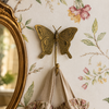 Single brass butterfly wall hook mounted on vintage floral wallpaper beside ornate gold mirror with delicate fabric hanging showing whimsical cottagecore nursery room styling. Handcrafted decorative coat hook from set of 4 for nursery room decor, girls room wall decor and baby shower gift. Unique gender reveal gift and new home housewarming gift for butterfly nursery and kids room decoration