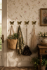 Wide lifestyle shot of four brass butterfly wall hooks mounted on vintage floral wallpaper entryway with woven bags, botanical plants and vintage dresser showing complete whimsical nursery and cottagecore wall transformation. Handcrafted decorative coat hook set for nursery room decor, kids room wall decor, baby shower gift and gender reveal gift. Unique new home housewarming gift for young families