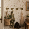 Set of four brass butterfly wall hooks mounted on vintage floral wallpaper beside door with woven bags and botanical plants hanging from hooks showing whimsical cottagecore entryway and nursery lifestyle styling. Handcrafted decorative coat hook set for nursery room decor, kids room decor, baby shower gift and housewarming gift. Unique gender reveal gift and new home gift for young families