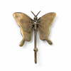 Angled view of brass butterfly wall hook on white background showing full wing detail, body texture, antenna and single hook arm with warm antique brass patina finish. Handcrafted whimsical decorative coat hook from set of 4 for nursery room decor, kids room wall decor and baby shower gift. Unique gender reveal gift and new home housewarming gift for butterfly nursery and girls room decoration