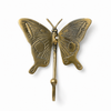 Brass butterfly wall hook isolated on white background showing full wing spread, intricate engraved surface detail, antenna and warm antique brass finish. Handcrafted whimsical decorative coat hook from set of 4 for nursery room decor, kids room wall decor and baby shower gift. Unique gender reveal gift, new home gift and housewarming gift for whimsical butterfly nursery and girls room decor