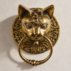 Brass cat head towel ring in polished gold on a cream wall, a detailed cat face with ornate Victorian scrollwork holding a solid brass ring. A handmade vintage towel ring and hand towel holder that also works as a gothic door knocker, a stylish cat lover gift hand-cast in Bali.