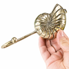 Side view of brass conch shell hook held in hand showing hook curve and depth