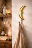 Gold brass crescent moon wall hook styled on a textured wall in a minimal celestial-themed room with warm lights and soft decor