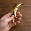 Hand holding polished gold brass crescent moon wall hook on wooden surface showing real life size and scale – part of celestial brass wall hook set of 3 – elegant hand-cast moon silhouette solid brass – witchy celestial boho decor – key hook jewelry holder – astrology gift – made in Bali