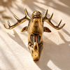 Low-angle view of the gold brass deer head hook on a sunlit wall, showing the full spread of the branching antlers above the hook. A striking antler wall decor piece and brass animal hook, handmade in Bali.
