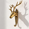 Brass deer head wall hook with branching antlers on a soft grey wall, casting a dramatic antler shadow. A handmade brass animal hook and deer wall hook from the brass deer, pine tree and maple leaf hook set of 3, cast in Ubud, Bali.