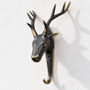 Brass deer head hook in a dark antique finish on a plain light wall, with branching antlers and a curved hook. A moody rustic cabin decor piece and stag hook, handmade in Ubud, Bali.