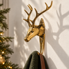 Brass deer head wall hook with antlers in polished gold, mounted beside a Christmas tree and holding a green knit stocking. A handmade stag hook used as a Christmas stocking holder, and a festive Christmas gift for deer lovers, cast in Bali.