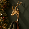 Gold brass deer wall hook on a dark green wall framed by Christmas garland, pinecones and red berries, holding a green stocking. A rustic cabin decor piece and stocking holder with branching antlers, handmade in Bali.