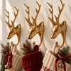 A row of brass deer stocking holders holding knit Christmas stockings in red, cream and green, decorated with pine sprigs, berries and jingle bells. Shows how several stag hooks hang the whole family's stockings, also available as a set of 4, handmade in Bali.