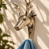 Brass deer wall hook holding a soft blue towel on a cream wall with leaf shadows, showing the stag's head and antlers in profile. A handmade towel hook and deer lover gift from Ubud, Bali.