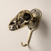 Solid brass dinosaur skull wall hook on a clean neutral background showing full sculpted skull face eye socket detail and single hook — gothic skull wall hook handmade in Ubud Bali