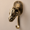 Solid brass dinosaur skull wall hook mounted on a warm beige wall showing three-quarter angled view of sculpted skull and hook — gothic dark academia wall hook handmade in Ubud Bali