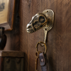 Solid brass dinosaur skull wall hook mounted on a dark wood wall with leather key fob hanging — gothic man cave key hook handmade in Ubud Bali
