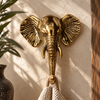Brass elephant wall hook in gold finish mounted on a green wall with a wood frame, holding a woven towel, boho home decor housewarming gift