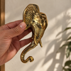 Hand holding a brass elephant wall hook in gold finish, showing trunk curl and hand cast detail