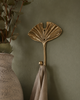 Gold brass fan leaf wall hook styled on warm olive green boho wall with soft linen cloth and natural accessories showing botanical nature-inspired interior styling. Handcrafted leaf shaped plant hanger hook, towel hook and coat hook for boho home decor, wabi sabi decor and housewarming gift for plant lovers and nature-inspired interiors