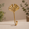 Gold brass fan leaf wall hook on warm neutral background showing full warm gold finish, intricate fan leaf vein detail and single hook arm. Handcrafted leaf shaped plant hanger hook, towel hook and coat hook for boho home decor, housewarming gift, nature-inspired entryway decor and botanical wall decor. Slow made in Bali from recycled brass