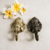 Two antique brass Ganesha wall hooks displayed with fresh white and yellow frangipani flowers showing rich dark patina finish and Balinese cultural artisan styling. Handcrafted Buddhist elephant wall hook for boho home decor, yoga room decor, meditation space and housewarming gift. Created respectfully by professional Hindu artisans in Bali. Available in gold finish too