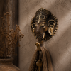 Close-up of antique brass Ganesha wall hook on warm neutral textured wall with decorative tassel hanging showing rich dark patina finish, intricate crown and elephant trunk detail. Handcrafted Buddhist Ganesha elephant wall hook for boho home decor, yoga room decor, meditation decor and housewarming gift. Created with reverence by professional Hindu artisans in Bali