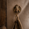 Antique brass Ganesha wall hook on dark moody wall with dramatic shadow showing deep dark patina finish and ornate Ganesha sculptural detail in eclectic interior styling. Handcrafted Buddhist elephant wall hook for boho home decor, eclectic decor, yoga room decor and housewarming gift. Created with reverence by professional Hindu artisans in Bali