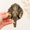 Hand holding large brass Ganesha wall hook in gold polished finish showing size scale, intricate crown and face detail and warm bright gold brass finish. Handcrafted Buddhist elephant wall hook for boho home decor, yoga room decor, meditation space and housewarming gift. Created respectfully by professional Hindu artisans in Bali. Available in small and large size