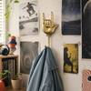 Brass hand gesture wall hook mounted in a music room holding a denim jacket, rock and roll coat hook for a man cave.