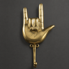 Brass hand gesture wall hook on a dark background, showing the detailed sign of the horns design and coat hook.