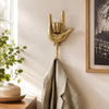 Brass hand gesture wall hook mounted on a wall holding a towel, handmade rock on coat hook and heavy metal decor.