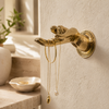 Brass hand wall hook holding necklaces near a bathroom sink, jewelry wall hook and cheeky statement decor.